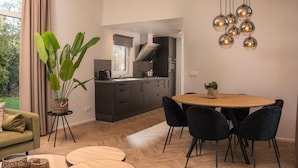 A modern kitchen with dark cabinets, a round wooden dining table, black chairs, and a hanging light fixture. - Vacation Home with Charming Porch (Zuna)
