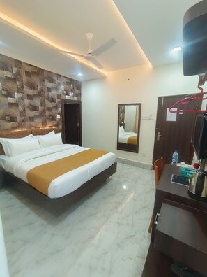 Habitación de hotel con cama, escritorio con hervidor, espejo y ventilador de techo.