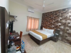 Una habitación de hotel con cama, escritorio con computadora, silla, armario, espejo, ventilador de techo y una pared con diseño decorativo.