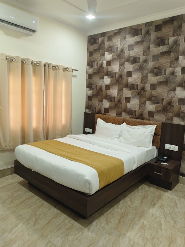 A hotel room with a bed, curtains, a wall with a geometric pattern, a ceiling light, and a nightstand with a phone.