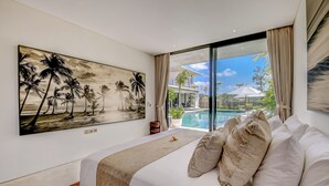 Un dormitorio con una cama grande, un cuadro de palmeras y vistas a una piscina y zona exterior.