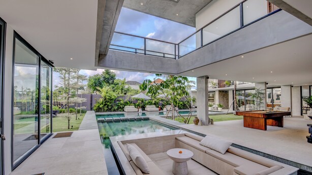 Un área de piscina interior moderna con pared de cristal, una sala de estar con una mesa y una mesa de billar.