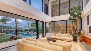 Un interior moderno con un sofá grande, una mesa de comedor y vistas a una piscina y zona exterior.