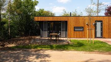 A modern wooden building with a paved entrance, a table and chairs outside, and a small tree nearby.