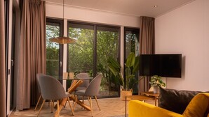 A modern living room with a sofa, chairs, a TV, and a large window with curtains. - Four-Person Bungalow in Overijssel (Zuna)