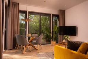 Een moderne woonkamer met een bank, stoelen, een televisie en een groot raam met gordijnen.