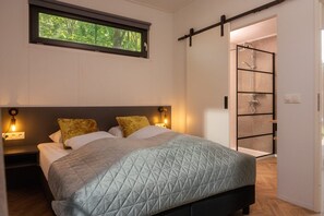 Een slaapkamer met een bed, een raam, een nachtkastje en een douche.