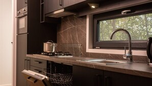 A modern kitchen with dark cabinetry, a built-in stove, a window above the sink, and a dishwasher. - Four-Person Bungalow in Overijssel (Zuna)