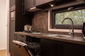 Une cuisine moderne avec des meubles de couleur sombre, une cuisinière encastrée, une fenêtre au-dessus de l’évier et un lave-vaisselle.
