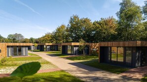 A modern building with a wooden exterior, glass doors, and a paved pathway leading to the entrance. - Four-Person Bungalow in Overijssel (Zuna)