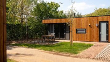 A modern building with a wooden exterior, a paved entrance, and a small outdoor seating area.