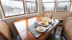 A dining table with breakfast items, a view of a snowy landscape through large windows, and wicker chairs.