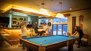 A pool table in a room with a bar area, chairs, and a view through a window.