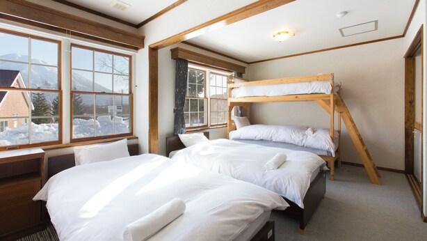 A room with two beds, a desk, and large windows with a view of snow-covered mountains.