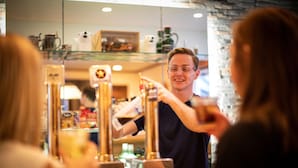 A bar area with a bartender serving drinks, a glass display case, and a counter.