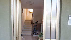 Un couloir menant à un escalier, avec un ventilateur de plafond, un distributeur d’eau et une plante en pot.