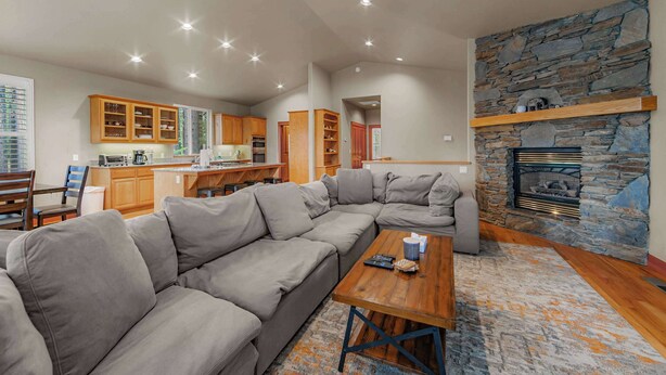 A modern living room with a sectional sofa, a fireplace, and a kitchen in the background. - Thunderbird Nest Hot Tub EV charger (South Lake Tahoe)
