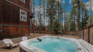 A hot tub in a backyard with wooden deck chairs, surrounded by tall trees. - Thunderbird Nest Hot Tub EV charger (South Lake Tahoe)