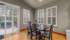 A dining area with a wooden table and chairs, large windows with blinds, and a ceiling light. - Thunderbird Nest Hot Tub EV charger (South Lake Tahoe)