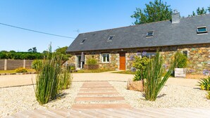 Une maison en pierre avec une allée en gravier et un chemin en bois menant à l’entrée.