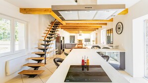 Une cuisine moderne avec un îlot central, un escalier en bois et une grande fenêtre.