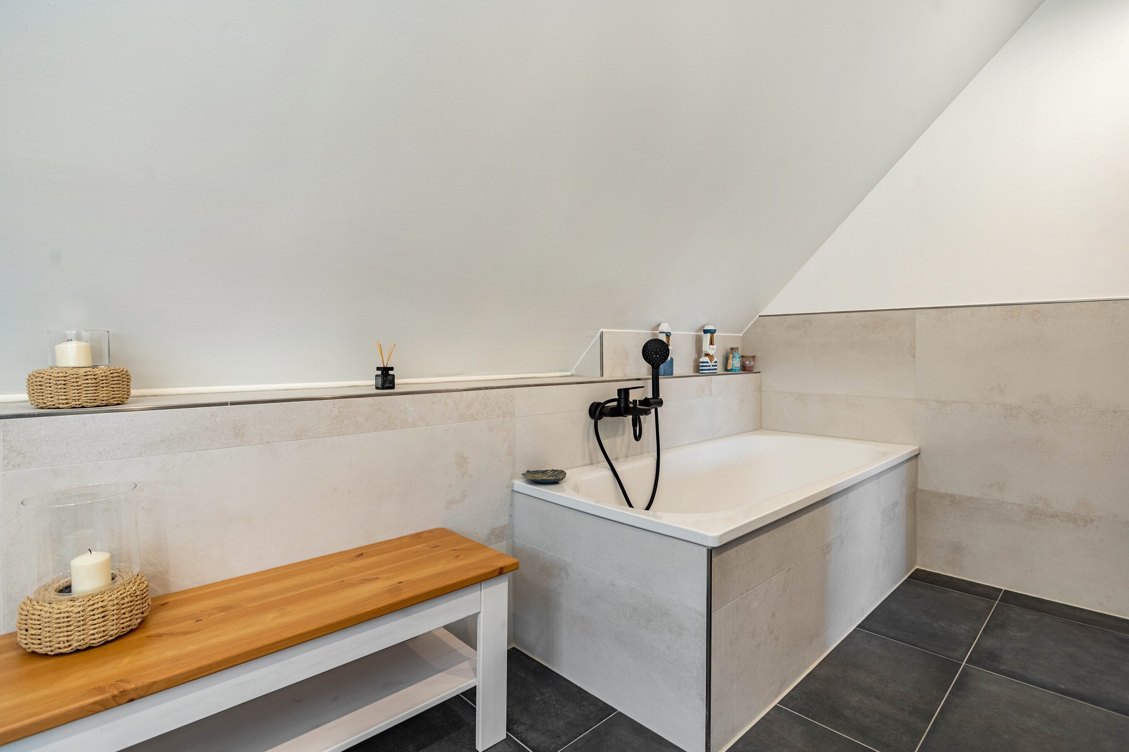 Un baño moderno con bañera, un banco de madera y una repisa con velas.