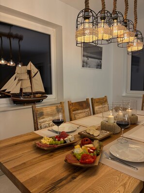 A dining table with a wooden finish, surrounded by chairs, a ship model, and a chandelier.