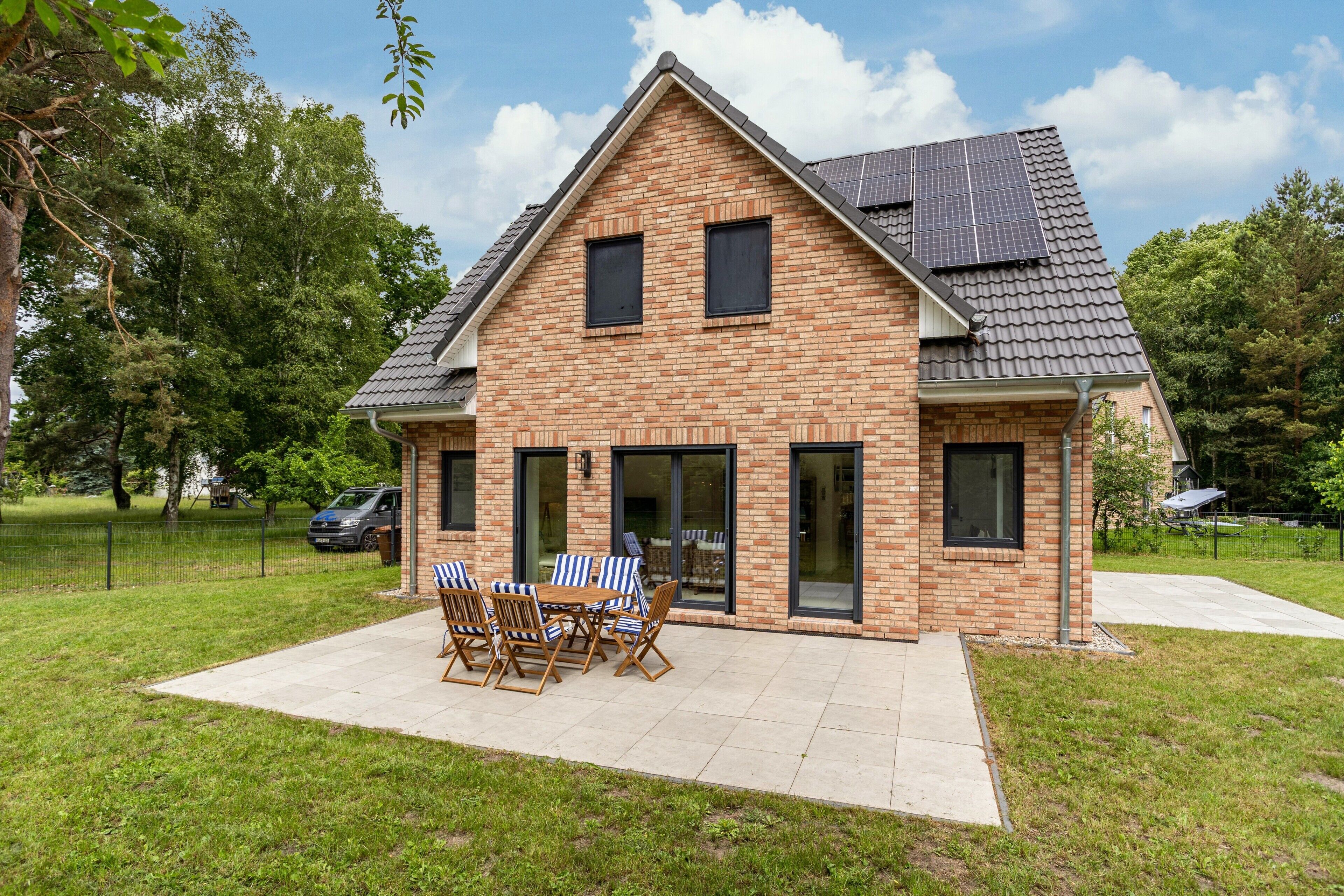 Ein zweistöckiges Haus mit Backsteinfassade, großen Fenstern und einer Terrasse mit Gartenmöbeln.