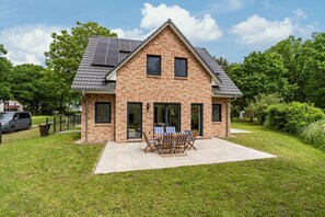 Ein zweigeschossiges Haus mit Ziegelaußenwand, großen Fenstern und einer Terrasse mit Gartenmöbeln.