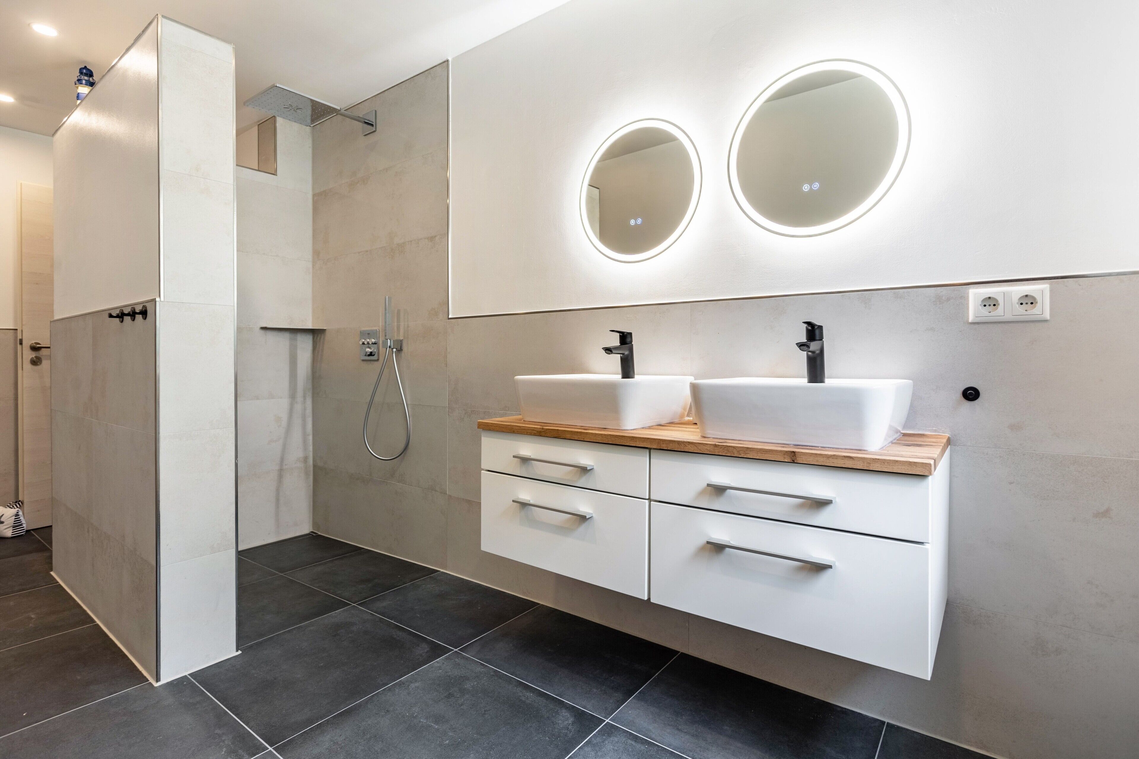 Ein modernes Badezimmer mit barrierefreier Dusche, zwei Waschbecken und einem Waschtisch mit Schubladen.