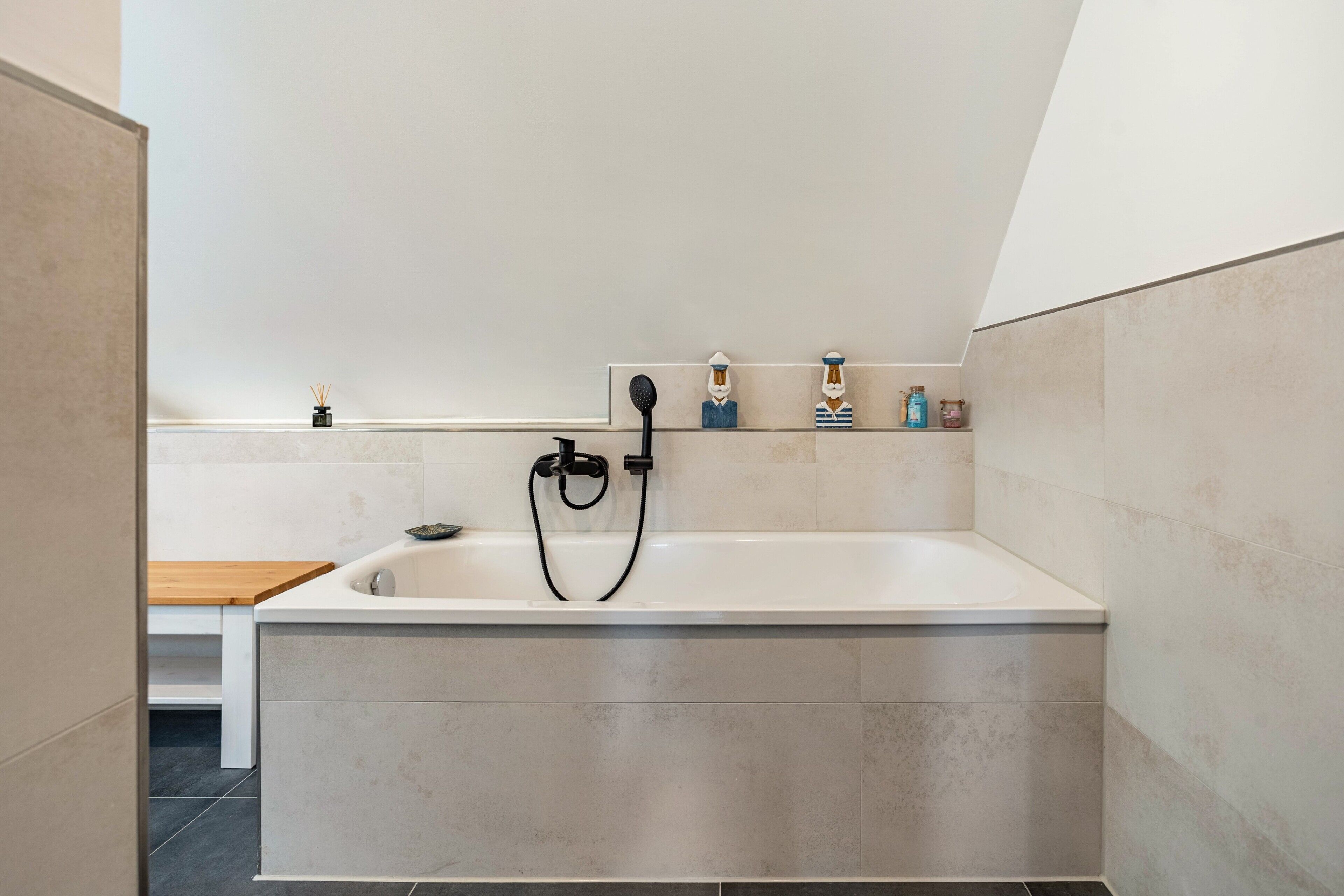 Ein modernes Badezimmer mit einer freistehenden Badewanne, einer Holzbank und einem Ablagebereich für Toilettenartikel.