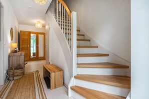 A staircase with wooden steps and white railings, a wooden bench, a rug, and a door leading to another room.