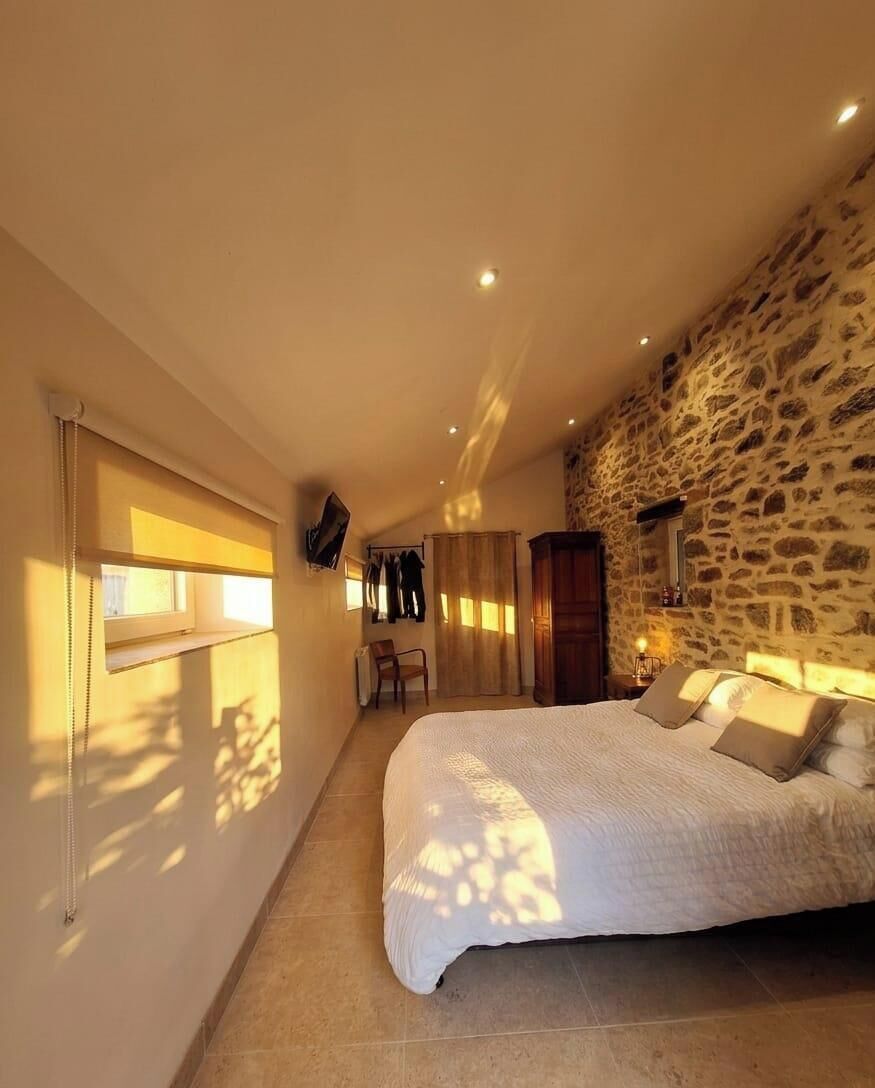 Une chambre à coucher avec un grand lit, un mur en pierre, un téléviseur fixé au mur et une fenêtre avec des rideaux.