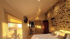 A bedroom with a large bed, a stone wall, a TV mounted on the wall, and a window with curtains. - "Parentezenn" cottage - for 15 people (Plésidy)