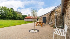 A rustic outdoor area with a gravel patio, a wooden picnic table, a white metal bench, and a stone building with a door. - "Parentezenn" cottage - for 15 people (Plésidy)