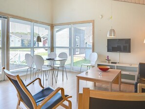 A modern living room with large windows, a flat-screen TV, and a dining area with a table and chairs. - 6 Person Holiday Park Home in Gudhjem (Gudhjem)