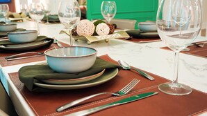 Une table à manger dressée avec des assiettes, des bols, des couverts et des verres à vin, avec une porte verte en arrière-plan.
