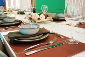 A dining table set with plates, bowls, cutlery, and wine glasses, with a green door in the background. - 5BR Themed Villa · Pool · Windsor Cay · Disney (Clermont)