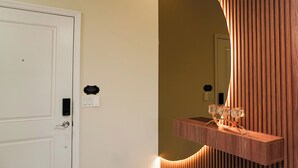 Une pièce avec une porte blanche, un luminaire fixé au mur et un miroir qui reflète une partie de la pièce.
