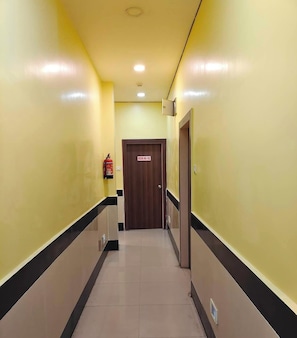 Un passadís amb un extintor, una porta amb la inscripció 'ROOM NO-102' i una lluminària al sostre.