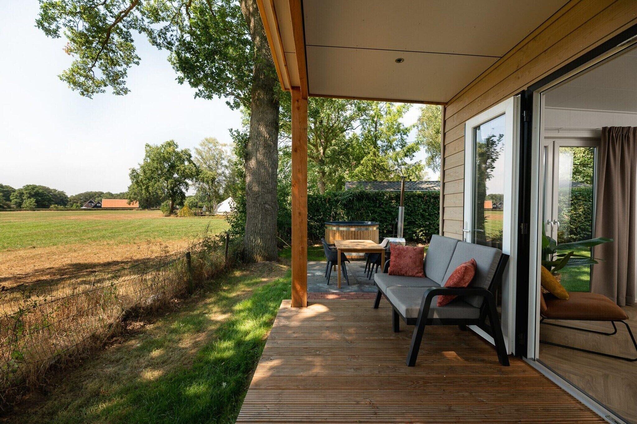 A covered outdoor seating area with a table and chairs, a sofa, and a view of a grassy field and trees.