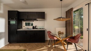 A modern kitchen with dark cabinets, a central island, and a dining area with a glass table and two chairs. - Cottage with Scenic Pasture Outlook (Zuna)
