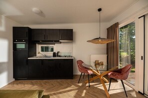 Une cuisine moderne avec des meubles de couleur sombre, un îlot central et un coin repas comprenant une table en verre et deux chaises.