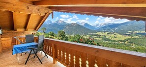 Un balcon en bois avec une table et une chaise, donnant sur un paysage montagneux.