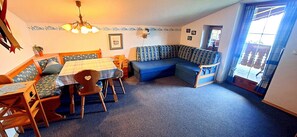 Ein gemütliches Zimmer mit Esstisch, Stühlen, einer Couch und einer Deckenleuchte.
