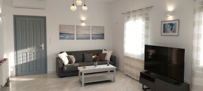 A living room with a sofa, coffee table, TV, and artwork on the wall. - Spacious apartment with sea view (Paros)