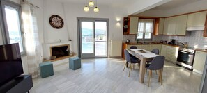 A modern kitchen with a dining area, a fireplace, and a view through the glass door. - Spacious apartment with sea view (Paros)