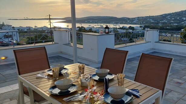 Terraço no telhado com mesa posta para refeições, com vista para uma cidade costeira e o mar.
