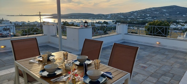 A rooftop terrace with a table set for dining, overlooking a coastal town and the sea. - Spacious apartment with sea view (Paros)