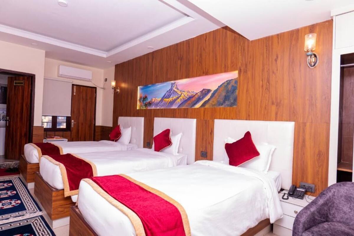 A hotel room with three beds, a painting on the wall, and a telephone on the nightstand.